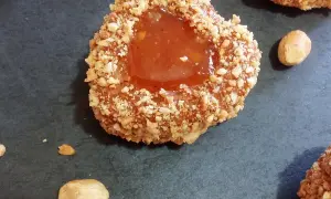 Un sablé algérien à la confiture, enrobé de noisettes concassées, sur fond sombre.