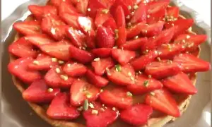 Tarte aux fraises fraîchement préparée, garnie de fraises coupées et de pistaches concassées. Un délice visuel et gustatif.