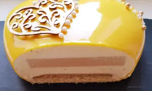 Entremet cœur jaune vif, décoré d'une arabesque dorée et de perles. La coupe révèle des couches onctueuses et un insert caramel beurre salé.