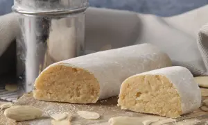 Pâte d'amande prête à être utilisée pour recouvrir un gâteau. Des amandes effilées et un tamis à sucre complètent cette scène gourmande.