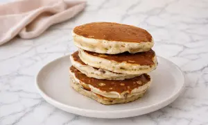 Pile de pancake banane moelleux sur une assiette, avec une serviette rose en arrière-plan.