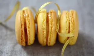 Trois macarons citron, parsemés d'un ruban doré scintillant. Une invitation à découvrir la recette macaron citron.