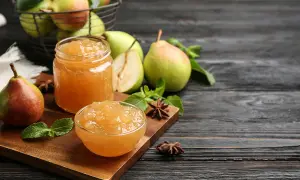 Confiture de poires dans un bocal et un bol, avec des poires fraîches et des feuilles de menthe sur une planche en bois.