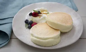 Deux pancakes aériens et moelleux saupoudrés de sucre glace, servis avec de la crème fouettée, des baies et du sirop.