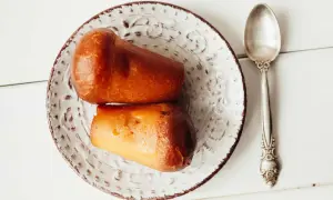 Deux baba au rhum dorés sur une assiette décorée, prêts à être dégustés avec une cuillère argentée.
