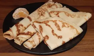 Crêpes dorées, roulées et pliées, sur une assiette noire, accompagnées de quelques quartiers d'orange. Un délice de crêpe sans oeuf.