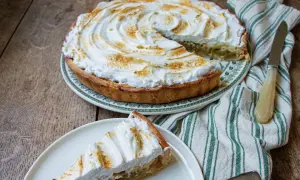 Une part de tarte rhubarbe meringuée, avec sa meringue dorée et sa garniture acidulée, sur une assiette blanche.