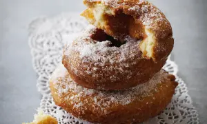 Un beignet au sucre, moelleux et doré, est empilé sur un autre, saupoudré de cristaux de sucre. Un morceau croqué révèle sa texture aérienne.
