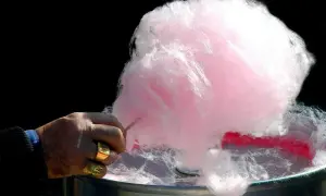 Main d'un homme fabriquant du sucre à barbe à papa rose et blanc.