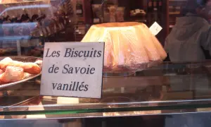 Un grand biscuit de Savoie vanillé, emballé sous plastique, est présenté dans une vitrine de boulangerie.