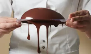 Comment faire du chocolat au lait : une demi-sphère de chocolat coule d'un moule transparent tenu par des mains.