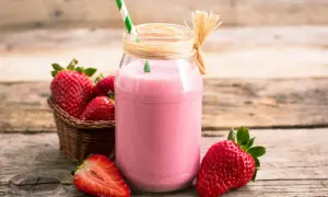 Un milkshake fraise glace, parfait pour une recette rafraîchissante. Des fraises fraîches dans un panier et une moitié de fraise sur la table.