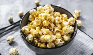 Un bol rempli de pop corn sucré, avec quelques grains éparpillés autour. Parfait pour une soirée cinéma gourmande.