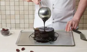 Un chef verse un glaçage miroir brillant sur un gâteau au chocolat.