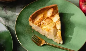 Une part de tarte normande aux pommes, dorée et appétissante, sur une assiette verte avec une fourchette dorée.