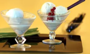 Deux coupes de **dessert glacé vanille** ornées de groseilles, sur un plateau sombre.