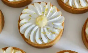 Plusieurs tartelettes au citron meringuées, décorées de zestes jaunes et d'une touche de meringue dorée. Un délice visuel pour un pochage tarte citron parfait.
