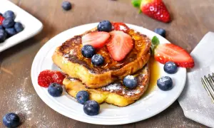Un délicieux pain perdu garni de fraises et de myrtilles, saupoudré de sucre glace. Un petit-déjeuner gourmand.