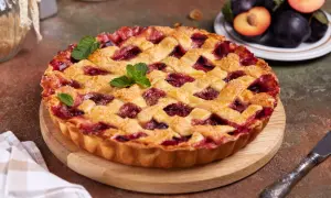Tarte aux prunes maison, avec une croûte dorée et une garniture généreuse de fruits rouges, décorée de feuilles de menthe.