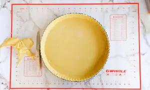 Préparation d'une conservation pâte brisée maison dans un moule à tarte, avec des chutes de pâte et un couteau.