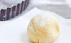 Une boule de pâte sucrée amande, saupoudrée de sucre glace, prête à être utilisée dans un moule à tarte.