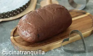 Pâte sablée au chocolat prête à être façonnée. Un emporte-pièce en forme de cœur est à proximité, suggérant de délicieuses créations.