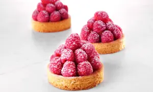 Trois tartelettes sablé breton garnies de framboises fraîches saupoudrées de sucre glace. Une invitation à la gourmandise.