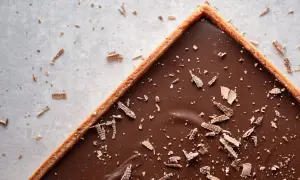 Une délicieuse tarte au chocolat vegan, garnie de copeaux de chocolat, sur un fond clair parsemé de miettes.