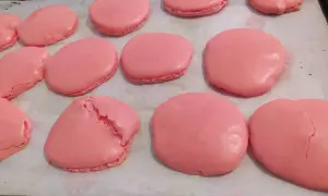 Coques de macarons roses sur une plaque de cuisson. Certaines sont parfaites, d'autres craquent, illustrant pourquoi les macarons craquent.