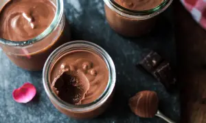 Trois pots de crème chocolat maison, on voit une cuillère avec une touche de mousse et des carrés de chocolat noir.