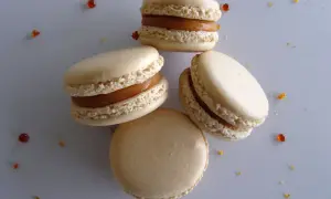 Quatre macarons au caramel beurre salé, parsemés de quelques éclats de caramel, sur fond gris.