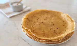 Pile de crêpes dorées, prêtes à être garnies. Une petite coupelle de sucre complète cette image évoquant la recette de pâte à crêpe parfaite.