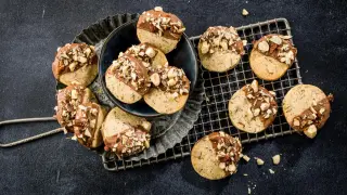 Des sablés aux noisettes, trempés dans du chocolat au lait et parsemés de morceaux de noisettes croquantes, sur un fond sombre.