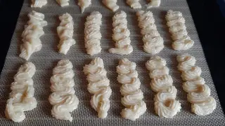 Pâte à spritz biscuits prête à cuire, disposée en rangées sur un tapis de cuisson.
