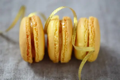 Trois macarons citron, parsemés d'un ruban doré scintillant. Une invitation à découvrir la recette macaron citron.