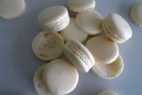 Des macarons blancs, certains assemblés, d'autres séparés, prêts pour la cuisson macaron chaleur tournante.