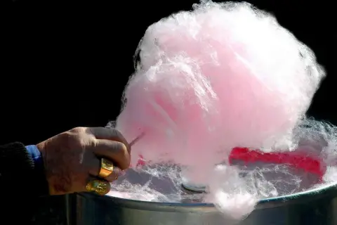 Main d'un homme fabriquant du sucre à barbe à papa rose et blanc.