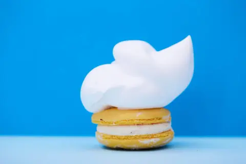 Un macaron jaune garni d'une crème blanche et surmonté d'une généreuse chantilly. Un délice qui rappelle la ganache chocolat macaron.