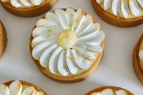 Plusieurs tartelettes au citron meringuées, décorées de zestes jaunes et d'une touche de meringue dorée. Un délice visuel pour un pochage tarte citron parfait.