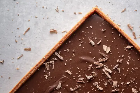 Une délicieuse tarte au chocolat vegan, garnie de copeaux de chocolat, sur un fond clair parsemé de miettes.