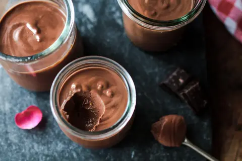 Trois pots de crème chocolat maison, on voit une cuillère avec une touche de mousse et des carrés de chocolat noir.