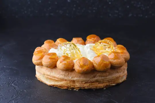 Un magnifique gâteau Saint-Honoré, avec ses choux caramélisés et sa crème aérienne, prêt à être dégusté.