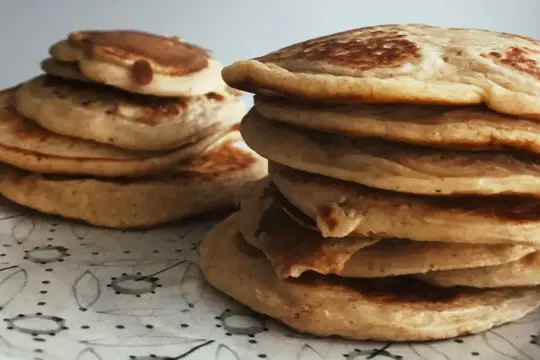 Deux piles de pancakes moelleux, parfaits pour une recette pancakes fluffy. Ils sont dorés et appétissants sur une assiette décorée.