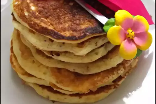 Pile de pancakes dorés, décorée d'une fleur en sucre et d'une serviette rouge. Parfait pour une recette pancakes réussie !
