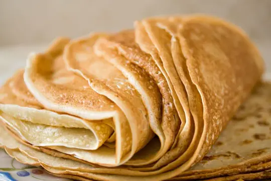 Pile de crêpes dorées, parfaites pour une recette pâte à crêpe facile. Elles sont empilées sur une assiette décorée.