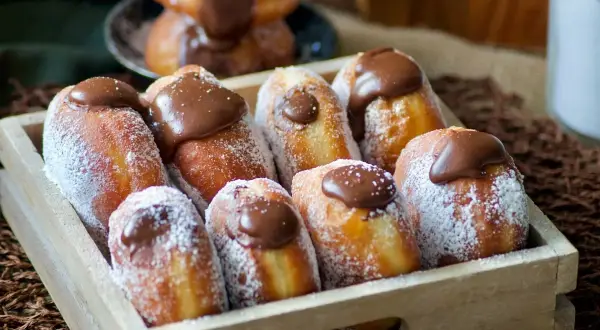 Un plateau en bois rempli de beignets au chocolat, saupoudrés de sucre glace. Un délice gourmand !