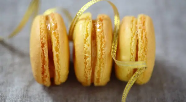Trois macarons citron, parsemés d'un ruban doré scintillant. Une invitation à découvrir la recette macaron citron.