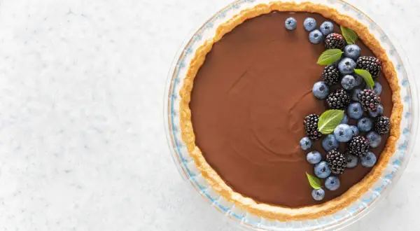 Une délicieuse tarte au chocolat au lait, garnie de myrtilles et de mûres fraîches, prête à être dégustée.