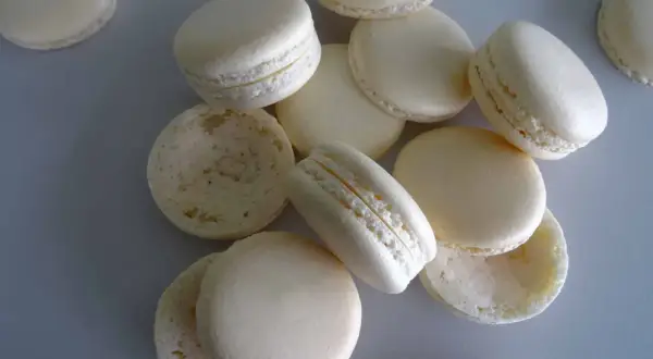 Des macarons blancs, certains assemblés, d'autres séparés, prêts pour la cuisson macaron chaleur tournante.