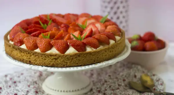 Tarte aux fraises sablé breton, garnie de crème pâtissière et de fraises fraîches, décorée de feuilles de menthe.